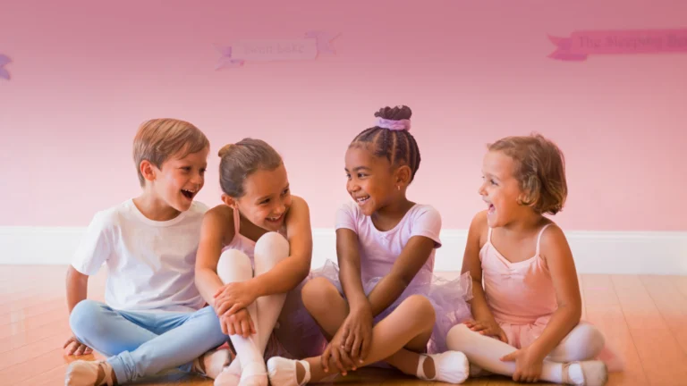 Smiling children sitting in a circle on a wooden dance floor at a studio offering toddler ballet classes in Elk Grove.